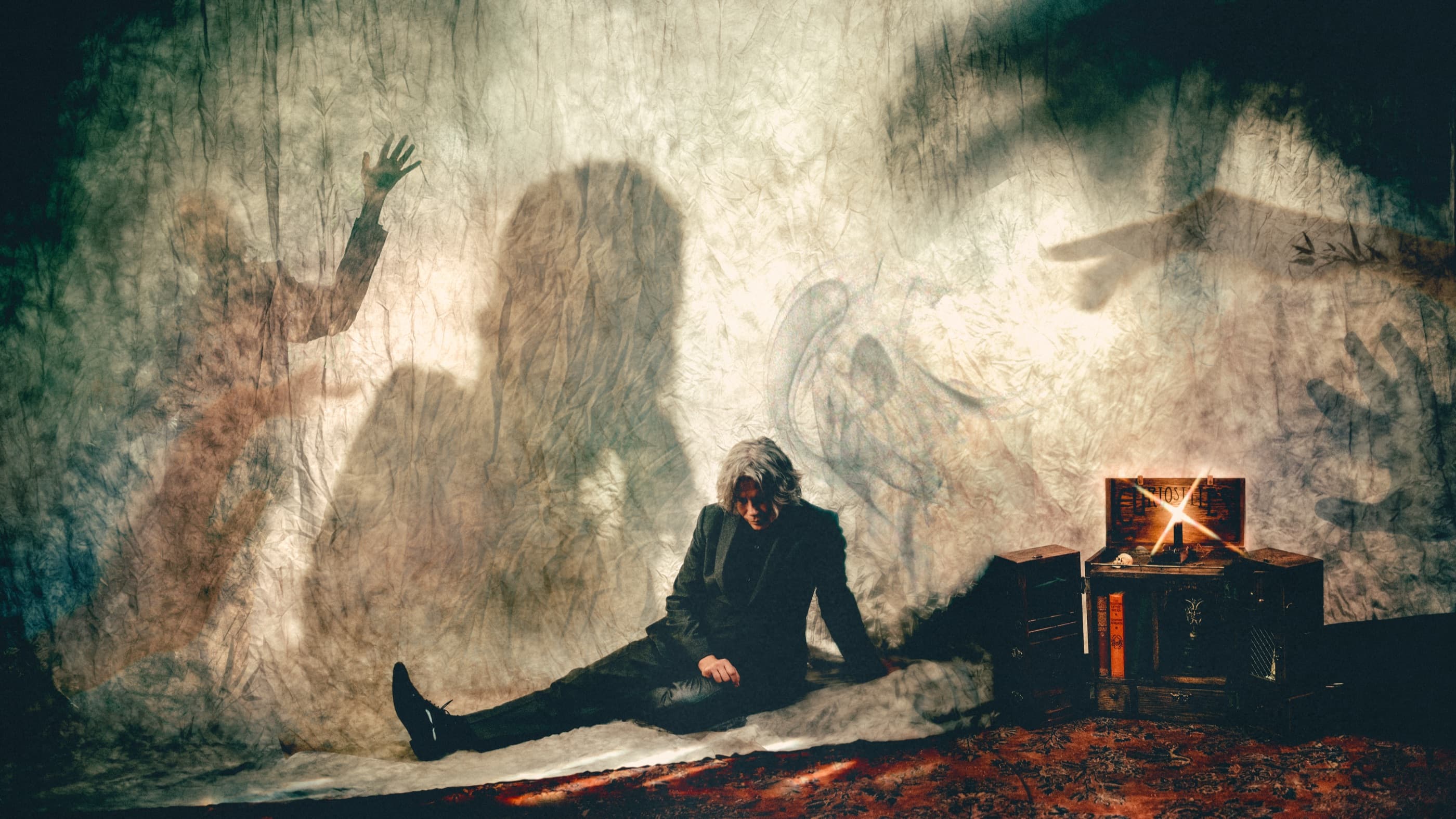 BC Smith sits beneath a wall of shadow figures beside a glowing chest.
