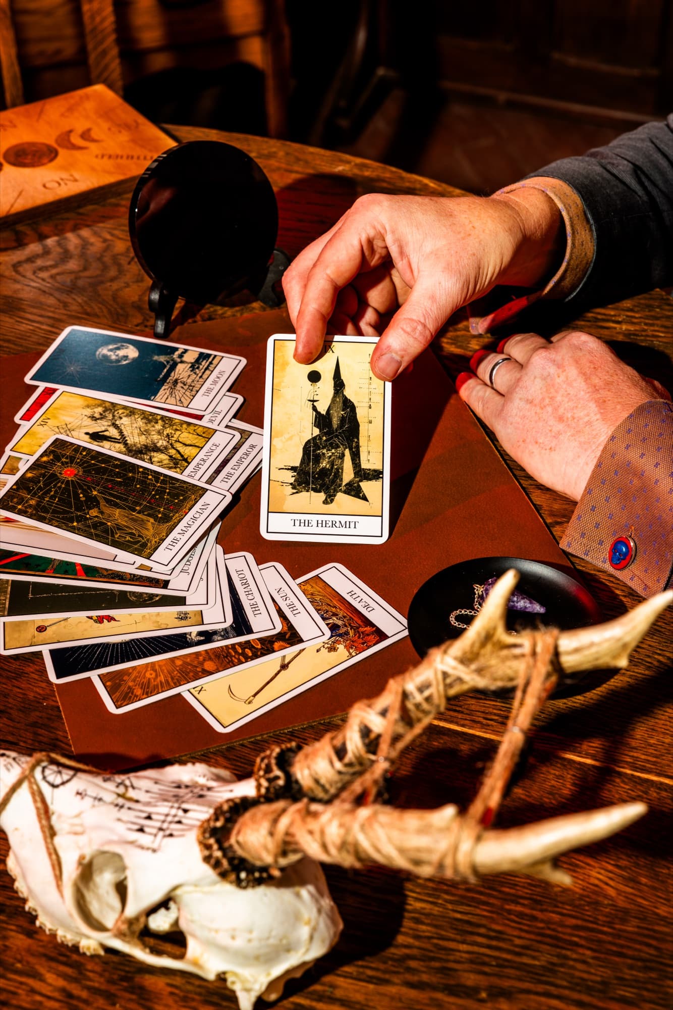 A hand draws The Hermit from a spread of tarot cards beside a carved skull.