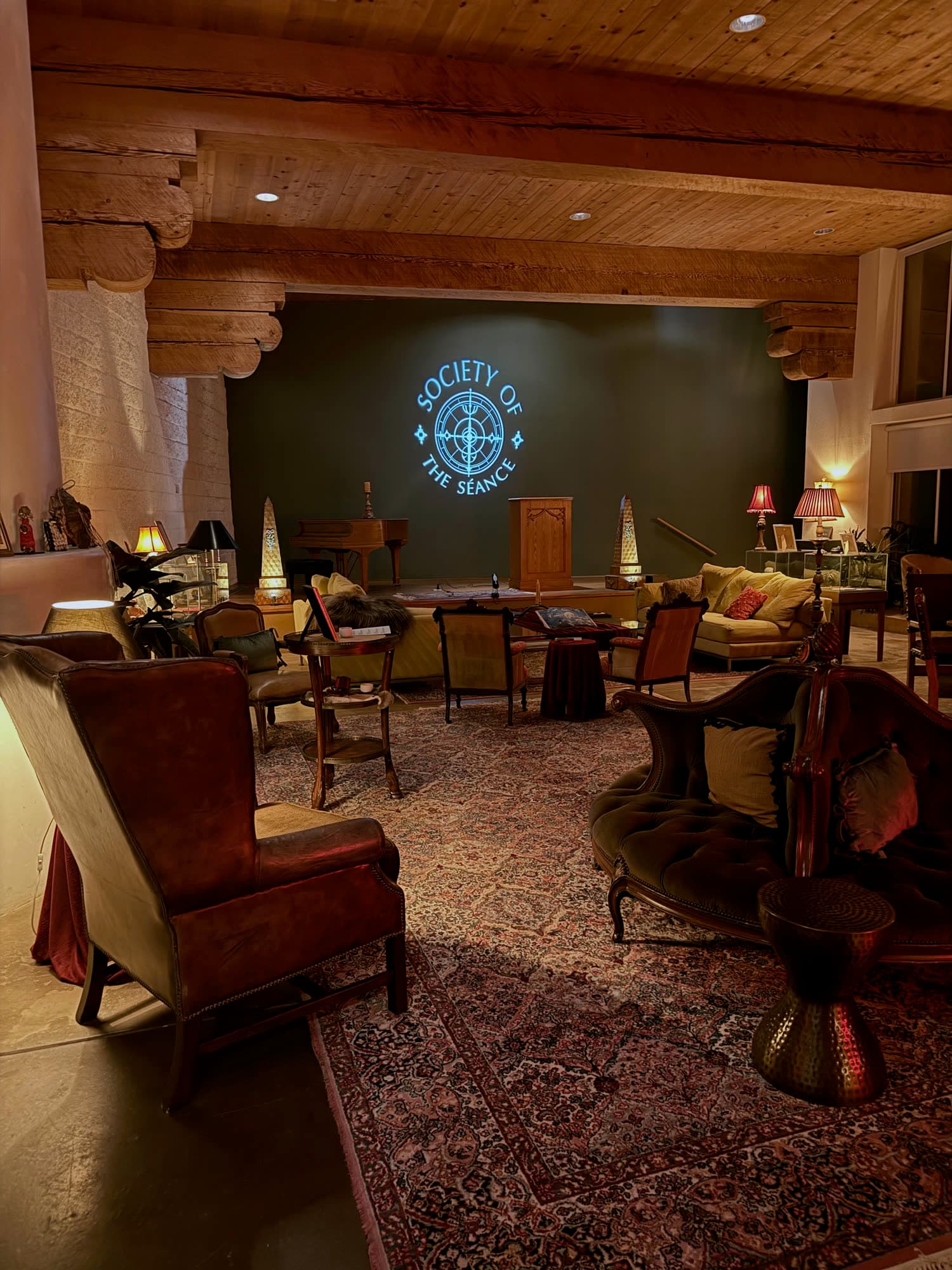 The Salon at night: a round tufted settee, armchairs, lamps and the Society of the Séance sign.
